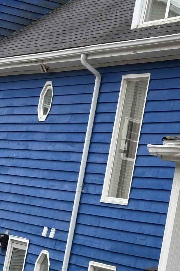 Gutters and downspout at Pier One after cleaning, white against the blue siding